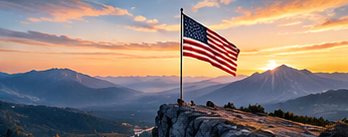 A flag on a rocky summit above mountains at sunrise